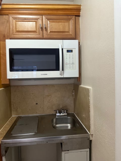 Kitchenette with wood cabinets, microwave, stone backsplash, and small sink — Yohandra’s Clearning Services, Miami
