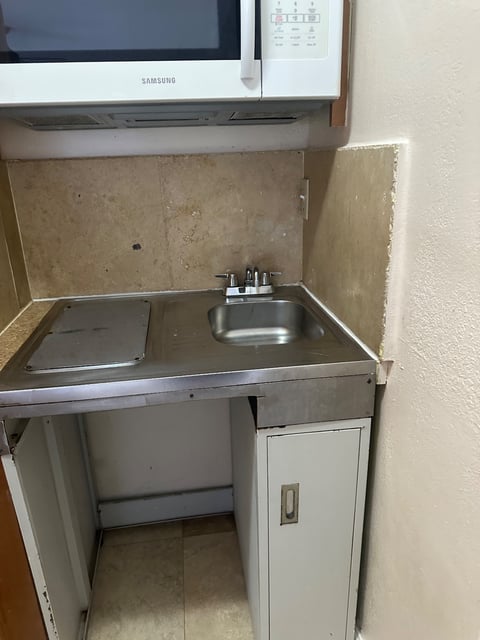 Small kitchenette with stainless sink, stovetop, and microwave above cabinets — Yohandra’s Clearning Services, Miami